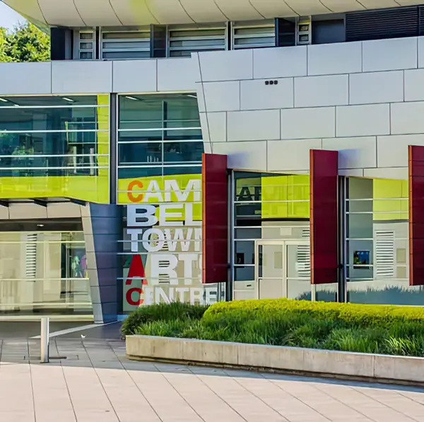 Modern building with curved white panels, large glass windows, and red vertical columns, labelled “Campbelltown Arts Centre,” near landscaped greenery—an architectural highlight in a vibrant area known for premium homesites and exciting new land development opportunities.