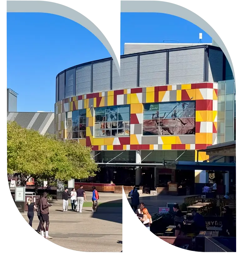 A modern building with colourful yellow and red panels, large windows, and people walking in an outdoor plaza—perfectly capturing the vibrant atmosphere of a new land development. This area highlights the excitement surrounding land release in Cambelltown, where premium homesites are set to complement the contemporary urban lifestyle.