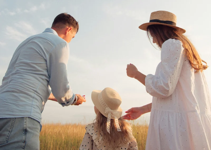 Two adults and a child wearing summer hats stand together in a field of tall grass, facing away from the camera on a sunny day—perhaps imagining their future as they explore new land development opportunities or Campbelltown land for sale.